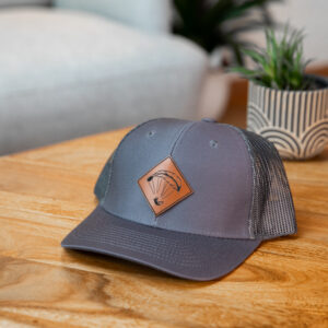 Graue Trucker Cap mit Kunstlederpatch mit stilisiertem Gleitschirm in Form einer Feder